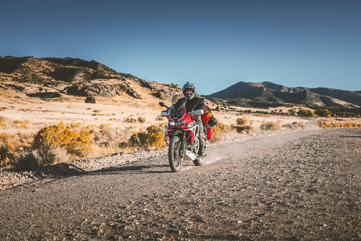A rider on a red motorcycle on a gravel road in a dry landscape