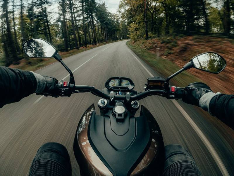 A rider's view over the handlebars of a motorcycle on a forest road
