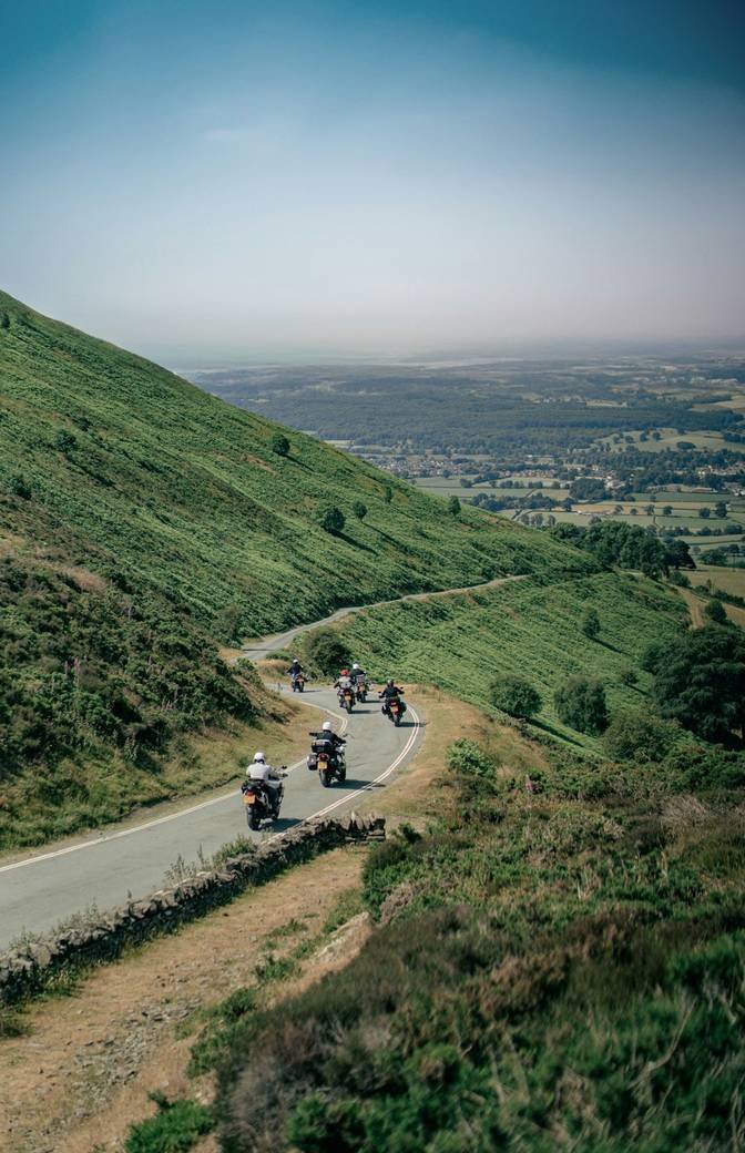 Motorcyclists riding a winding road through green hills