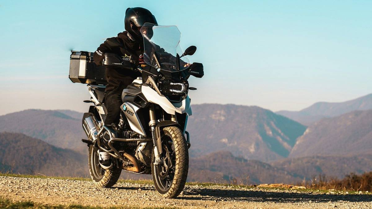A rider on an adventure touring motorcycle with luggage, parked above a mountain valley